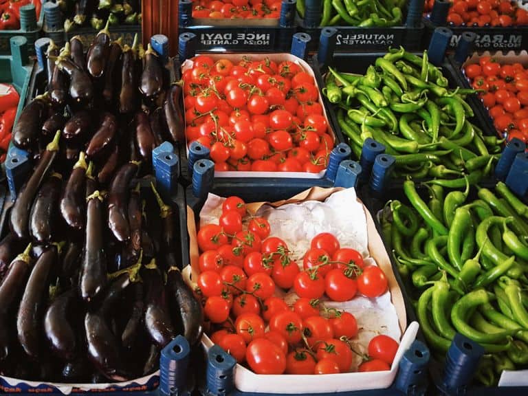 Vibrant display of fresh eggplants, tomatoes, and peppers at a bustling market. Perfect for lifestyle and food themes.