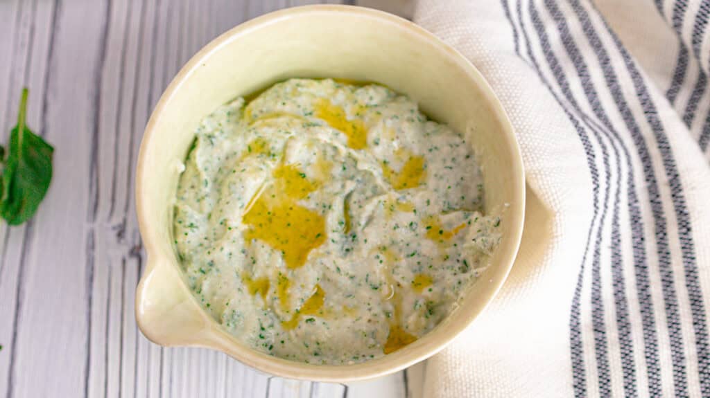 Whipped basil lemon ricotta dip on a board with a blue striped tea towel.